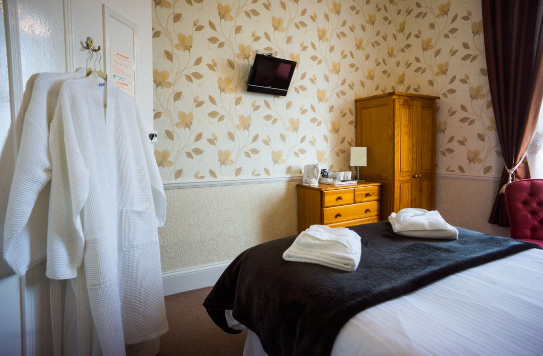 A hotel room with a bed, a wooden wardrobe, a television mounted on the wall, and a set of towels on the bed.