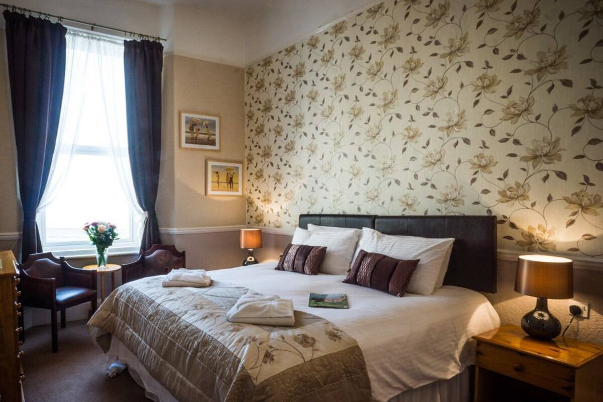A hotel room with a large bed, two bedside tables, a chair, a desk, and a window with curtains.