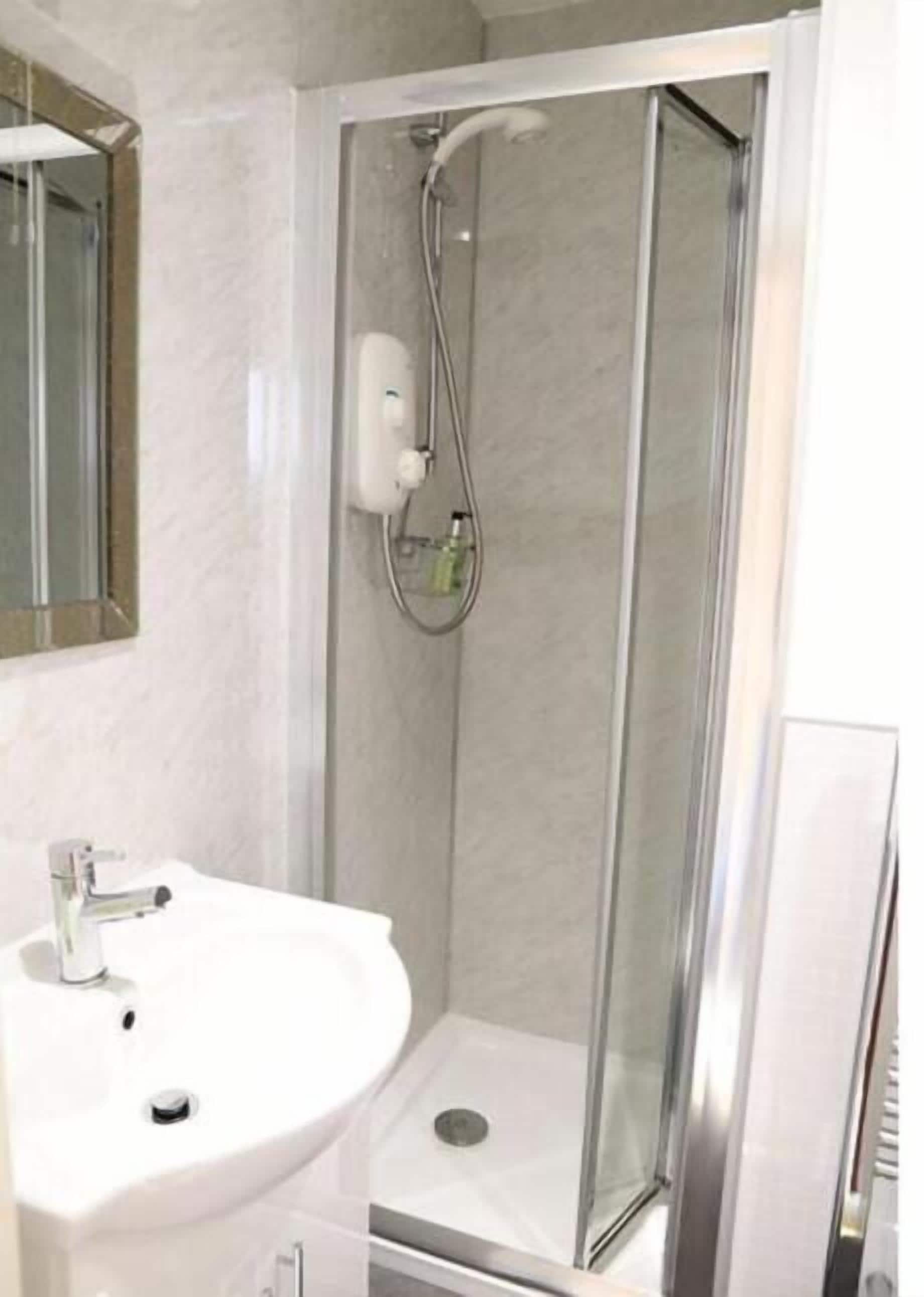 A modern bathroom with a glass-enclosed shower, a white sink, and a mirror above the sink.