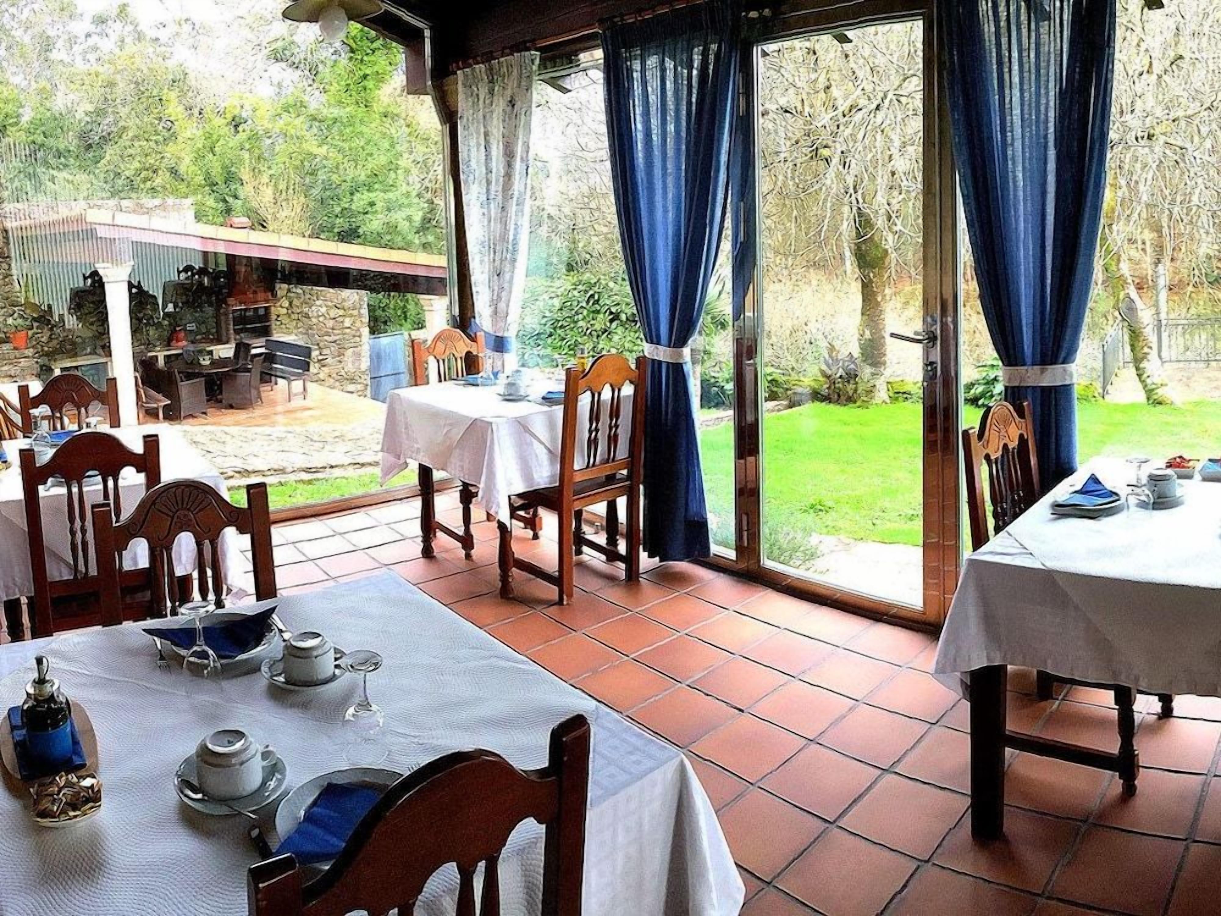 Un comedor al aire libre con mesas y sillas, vistas al jardín y una zona de estar cubierta.