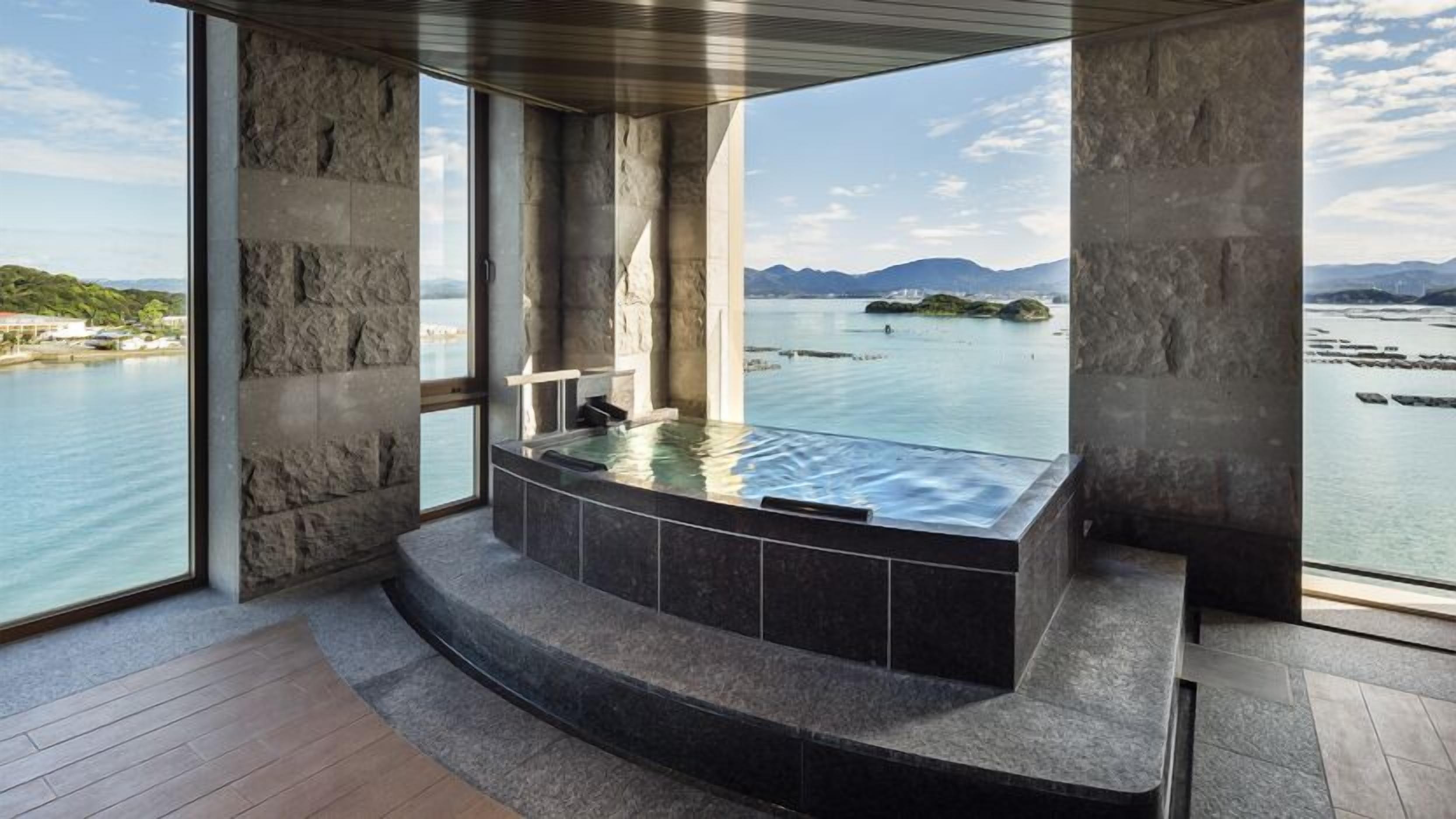 Un espace spa doté d’un jacuzzi, de murs en pierre et offrant une vue sur un plan d’eau et des montagnes.
