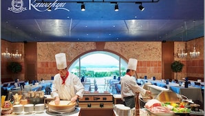 A restaurant with chefs preparing food, a view of greenery through a large window, and a ceiling with recessed lighting. - Hotel Kawakyu (Shirahama)