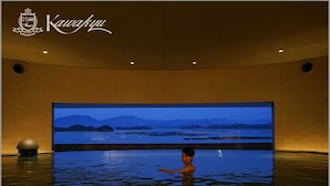 A person in a large indoor pool with a view of mountains and water. - Hotel Kawakyu (Shirahama)