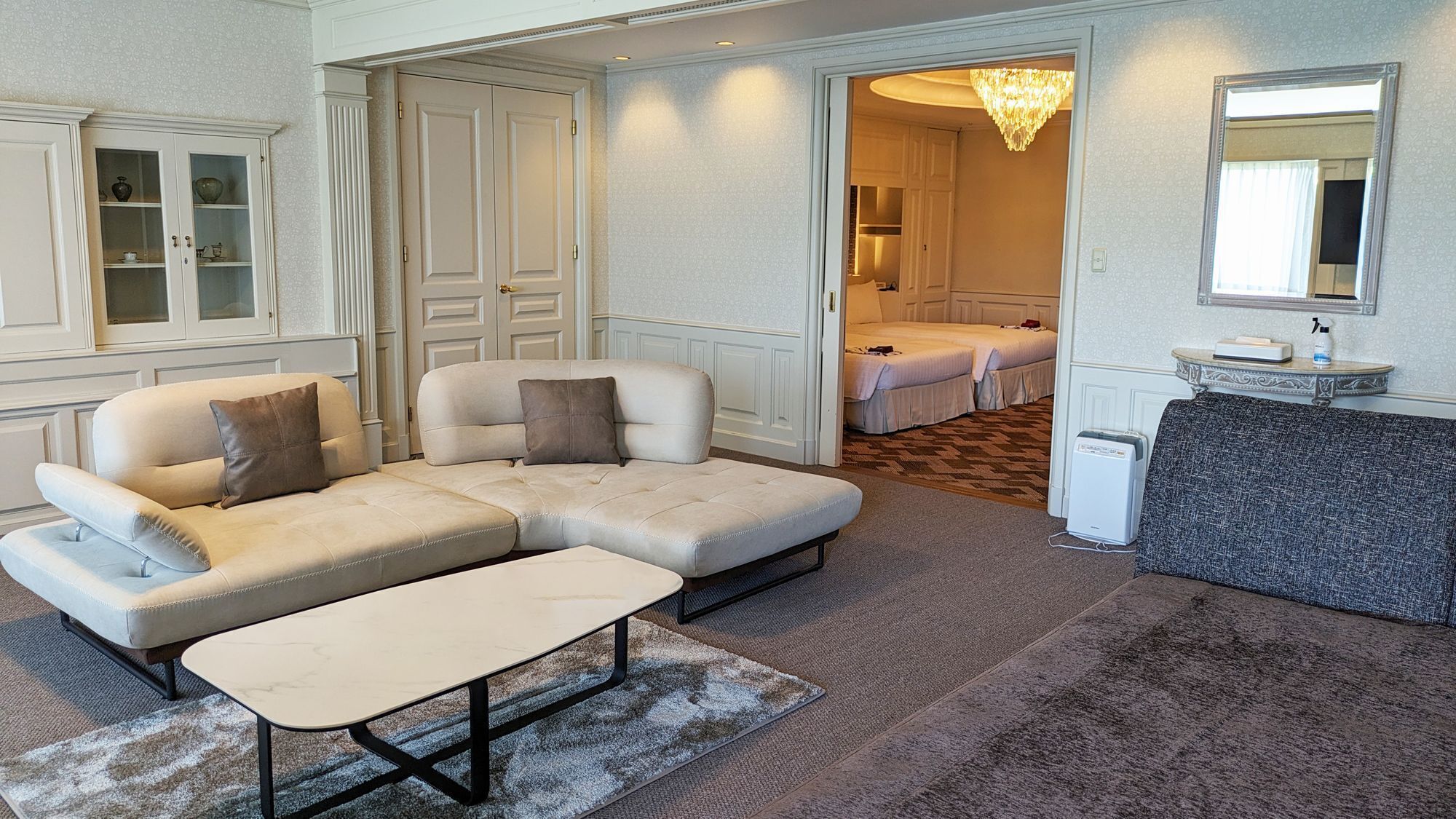 Un salon moderne avec un canapé d’angle, une petite table et un couloir menant à une chambre.
