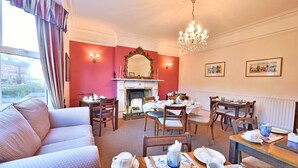 A dining area with a fireplace, dining table set for four, and a sofa in the foreground. - Virginia Lodge (Stratford-upon-Avon)