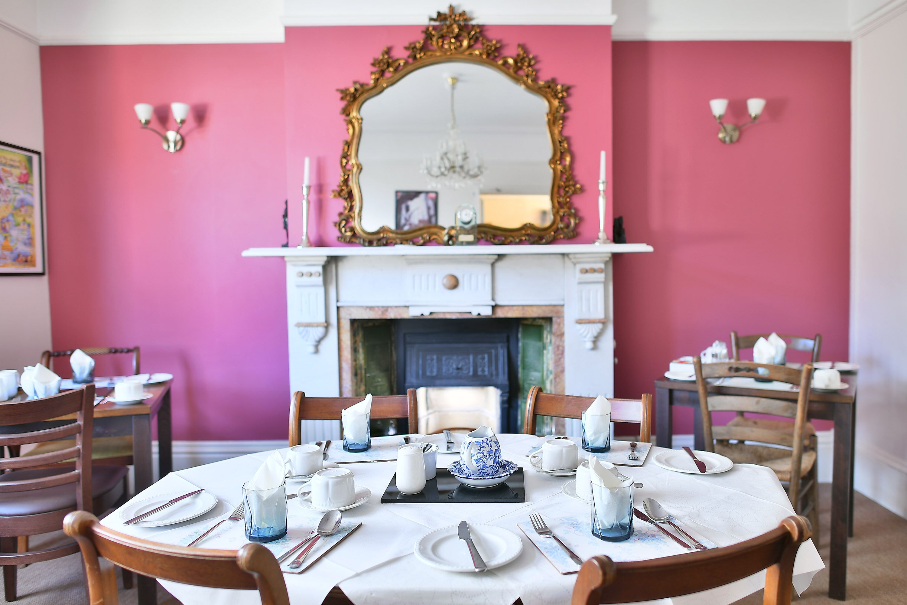 A dining room with pink walls, a fireplace, and a mirror above it.