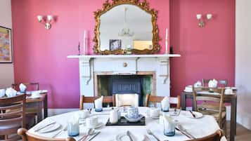 A dining room with pink walls, a fireplace, and a mirror above it.