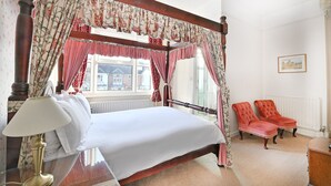 A bedroom with a four-poster bed, a mirror, a lamp, two armchairs, and a window with curtains. - Virginia Lodge (Stratford-upon-Avon)