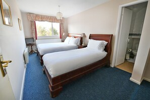 A hotel room with two single beds, a desk with a laptop, a window with curtains, and a shower area. - Virginia Lodge (Stratford-upon-Avon)