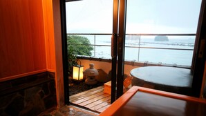 A traditional Japanese room with a stone fireplace, a wooden bench, and a view of the sea through a sliding door. - Kochoran (Toba)