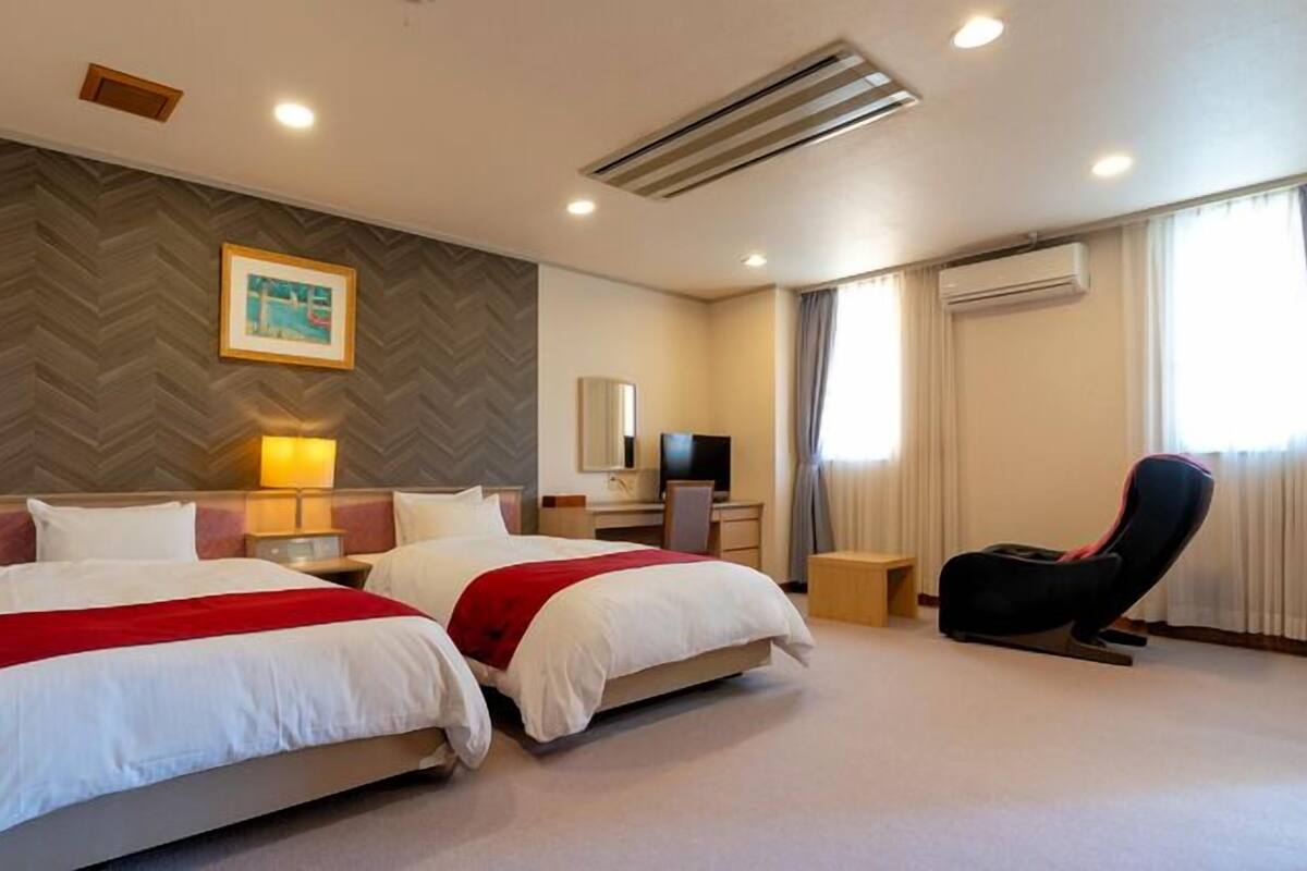 A hotel room with two beds, a desk, a chair, a TV, and a painting on the wall.