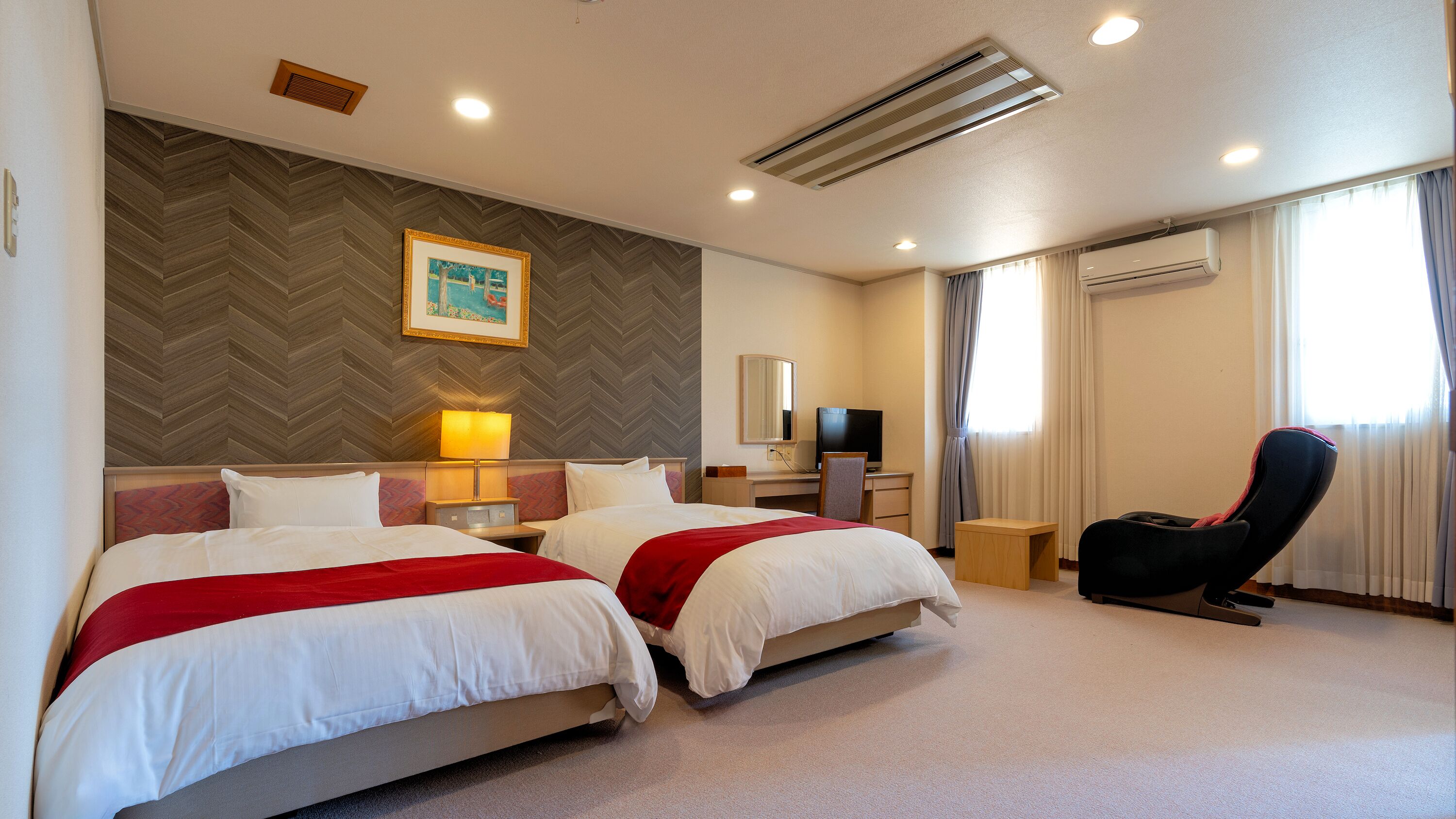 A hotel room with two beds, a desk, a chair, a TV, and an air conditioning unit.