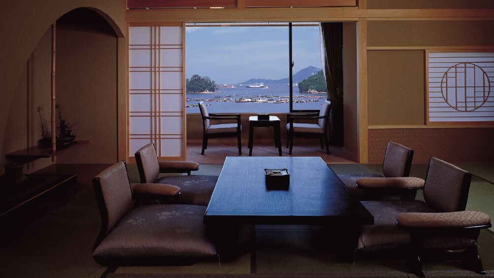 A room with a large table and chairs, a view of the sea, and traditional Japanese sliding doors.