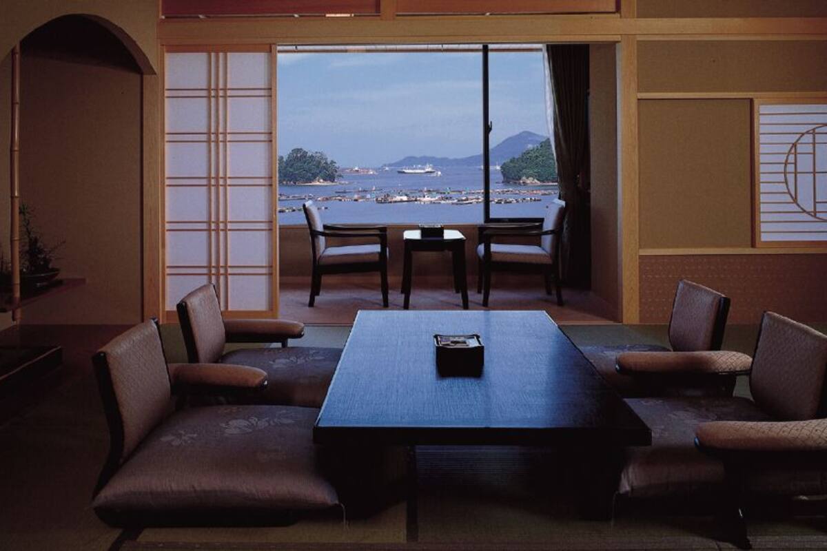 A room with a large table and chairs, a view of the sea, and traditional Japanese sliding doors.