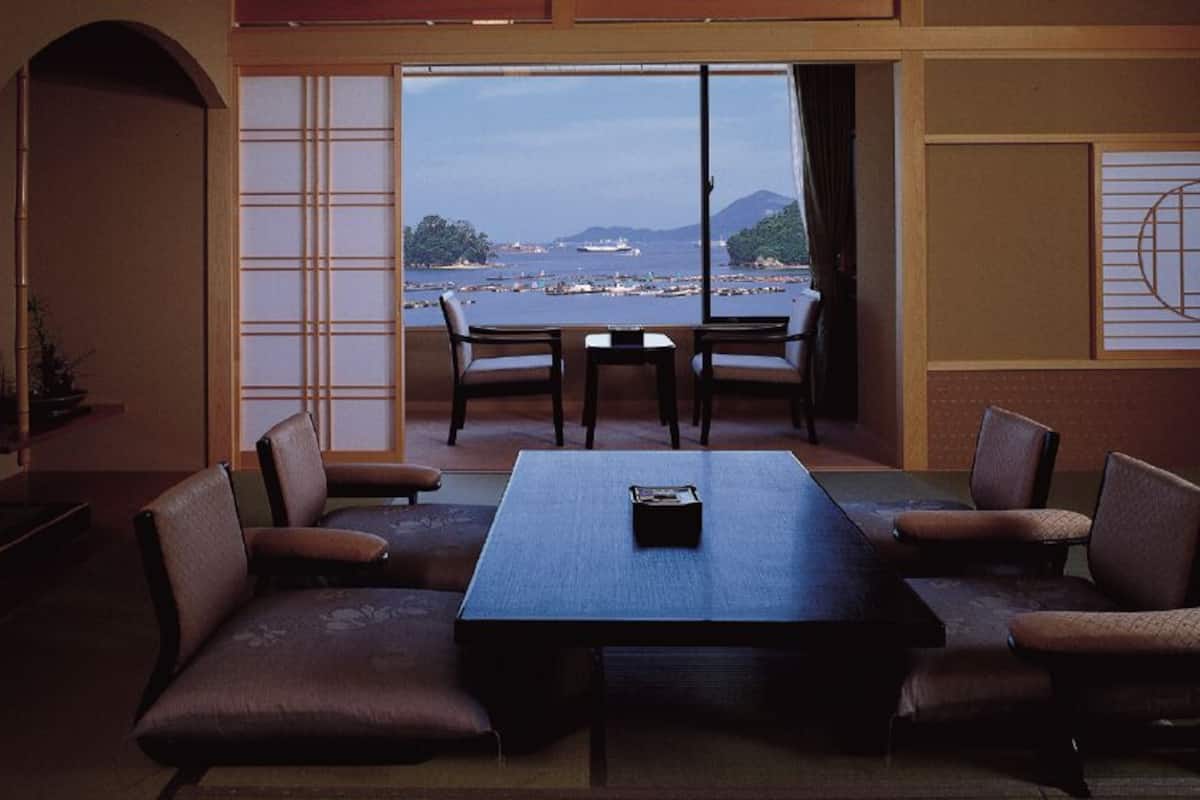 Una habitación con una mesa grande y sillas, vista al mar y puertas correderas tradicionales japonesas.