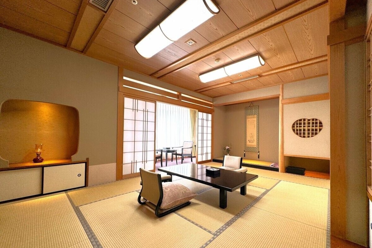 Una habitación tradicional japonesa con suelo de tatami, una mesa baja, sillas y puertas correderas.