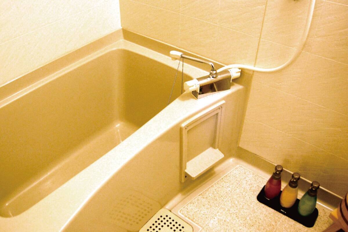 A bathtub with a showerhead, a small shelf, and a step leading into the tub.