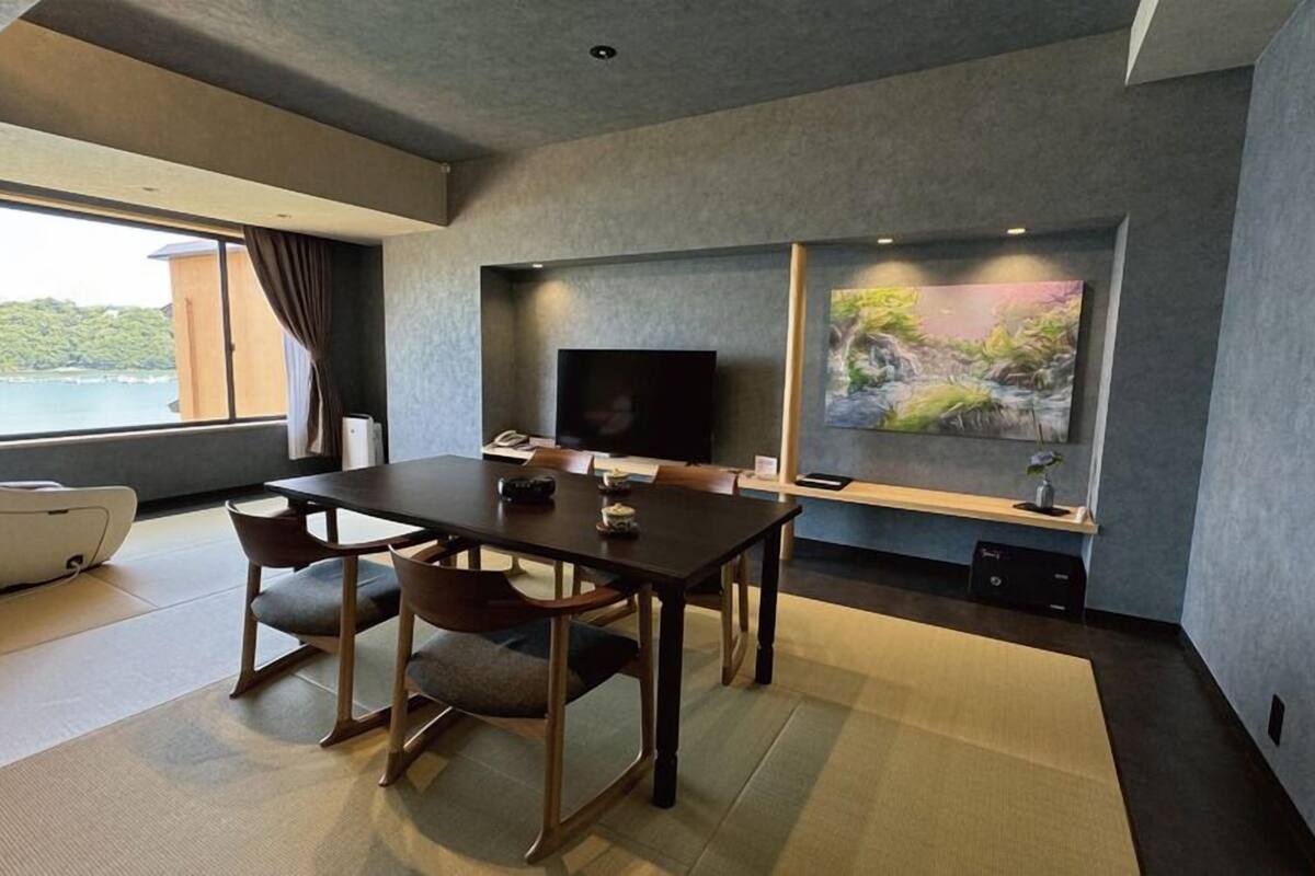 A modern room with a dining table, chairs, a flat-screen TV, a painting, and a view of the outdoors.
