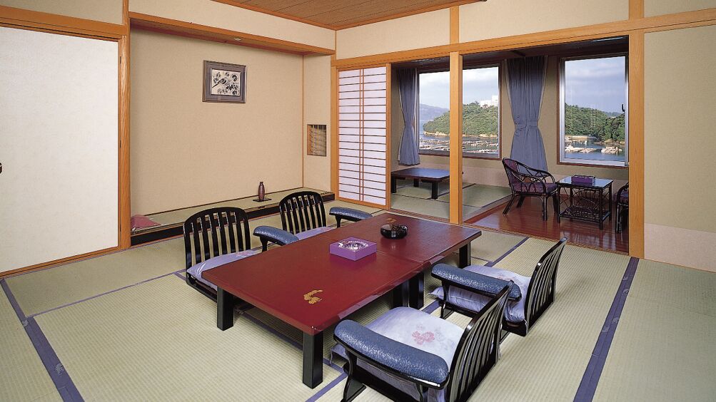 A tatami mat room with a low table and chairs, a sliding door, and a view of a mountainous landscape.