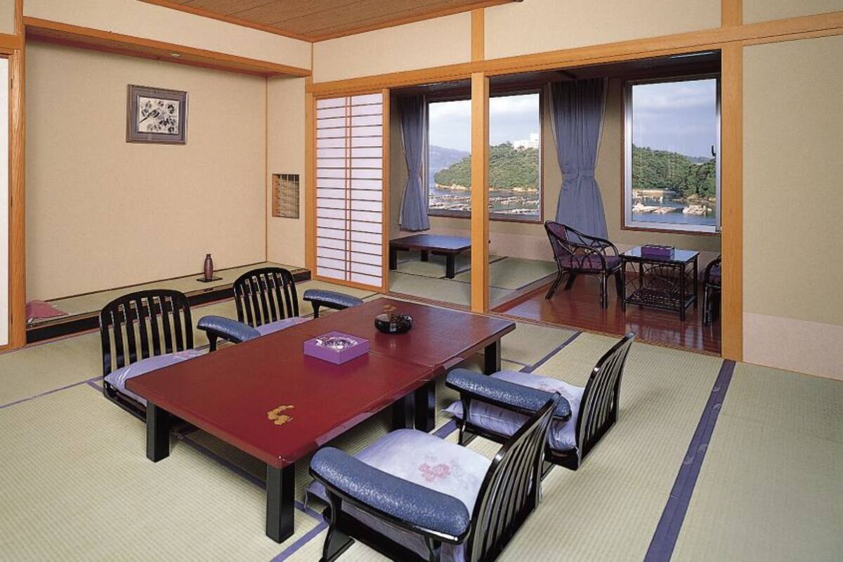 A tatami mat room with a low table and chairs, a sliding door, and a view of a mountainous landscape.