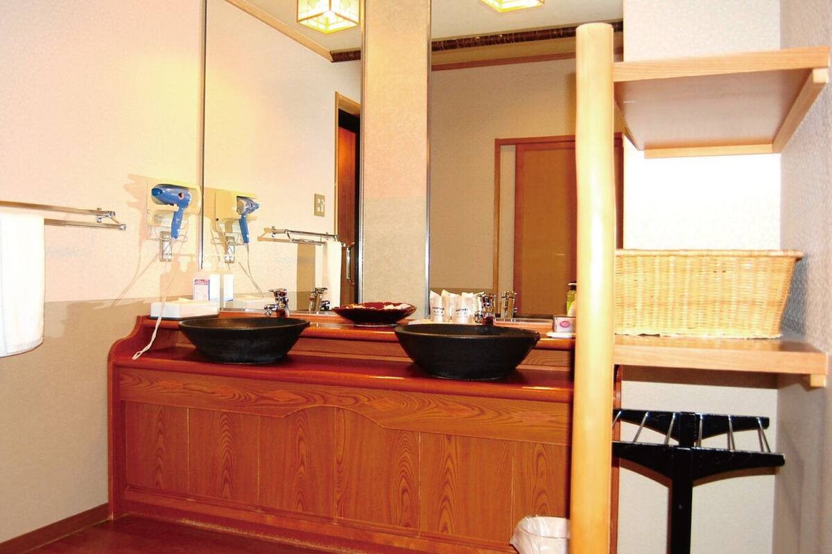 A bathroom with a wooden vanity, two sinks with black bowls, a towel rack, a mirror, and a shelf with a basket.