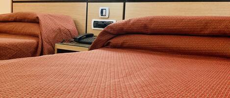 Habitación de hotel con una cama grande, una mesita de noche con teléfono y un termostato en la pared.