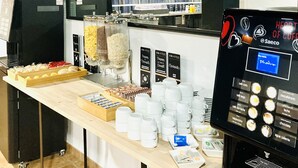 Een koffiehoek met een koffieapparaat, een etalage met eten en een zithoek.