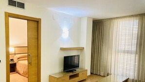 Een hotelkamer met een houten deur, een televisie op een houten standaard, een glazen tafel en een rode bank.