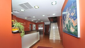 A hotel reception area with a wooden floor, a reception desk, a staircase, and a large wall painting. - Hostal Goyma III (San Fernando de Henares)