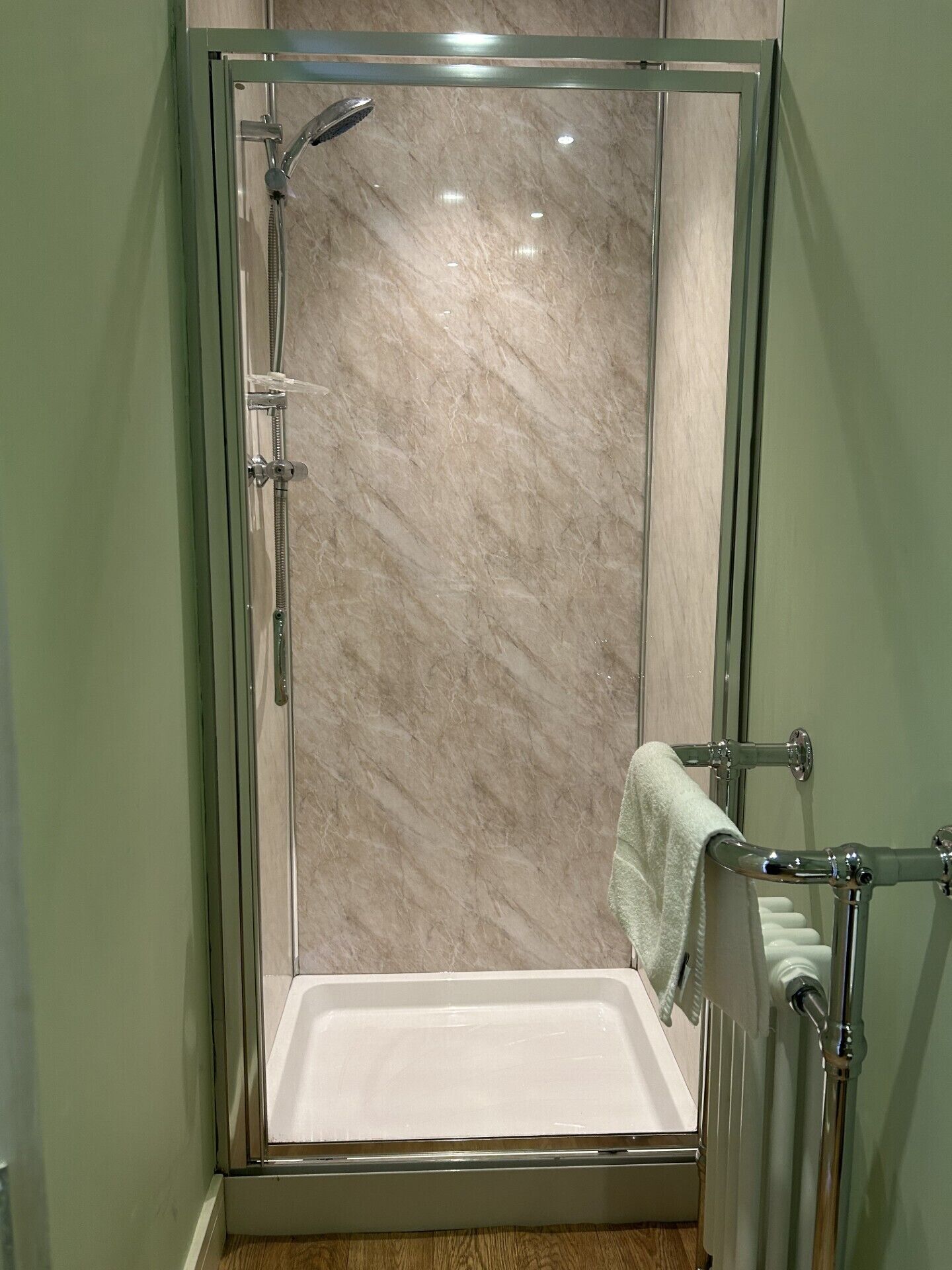 A glass-enclosed shower stall with a white bathtub, a towel rack, and a visible towel.