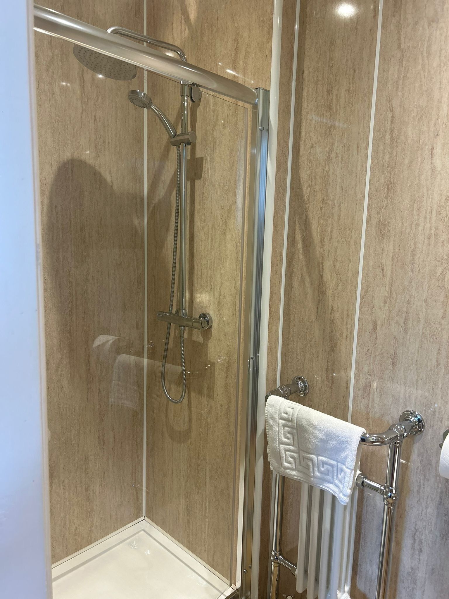 A glass-enclosed shower with a handheld showerhead and a handheld shower attachment.