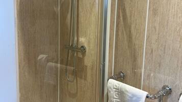 A glass-enclosed shower with a handheld showerhead and a handheld shower attachment.