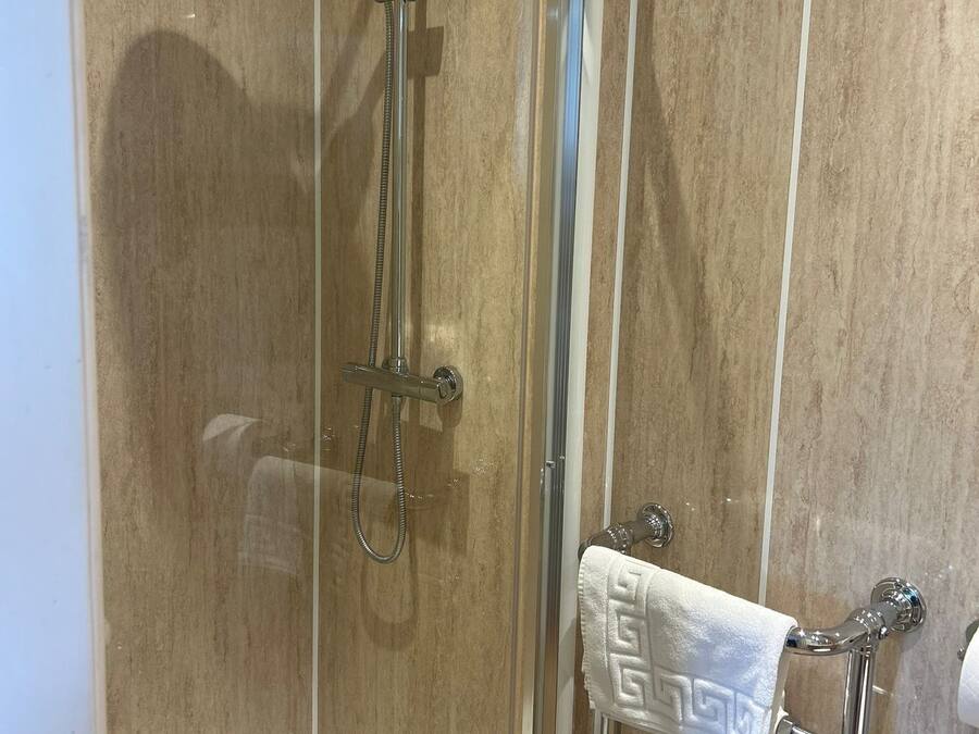 A glass-enclosed shower with a handheld showerhead and a handheld shower attachment.