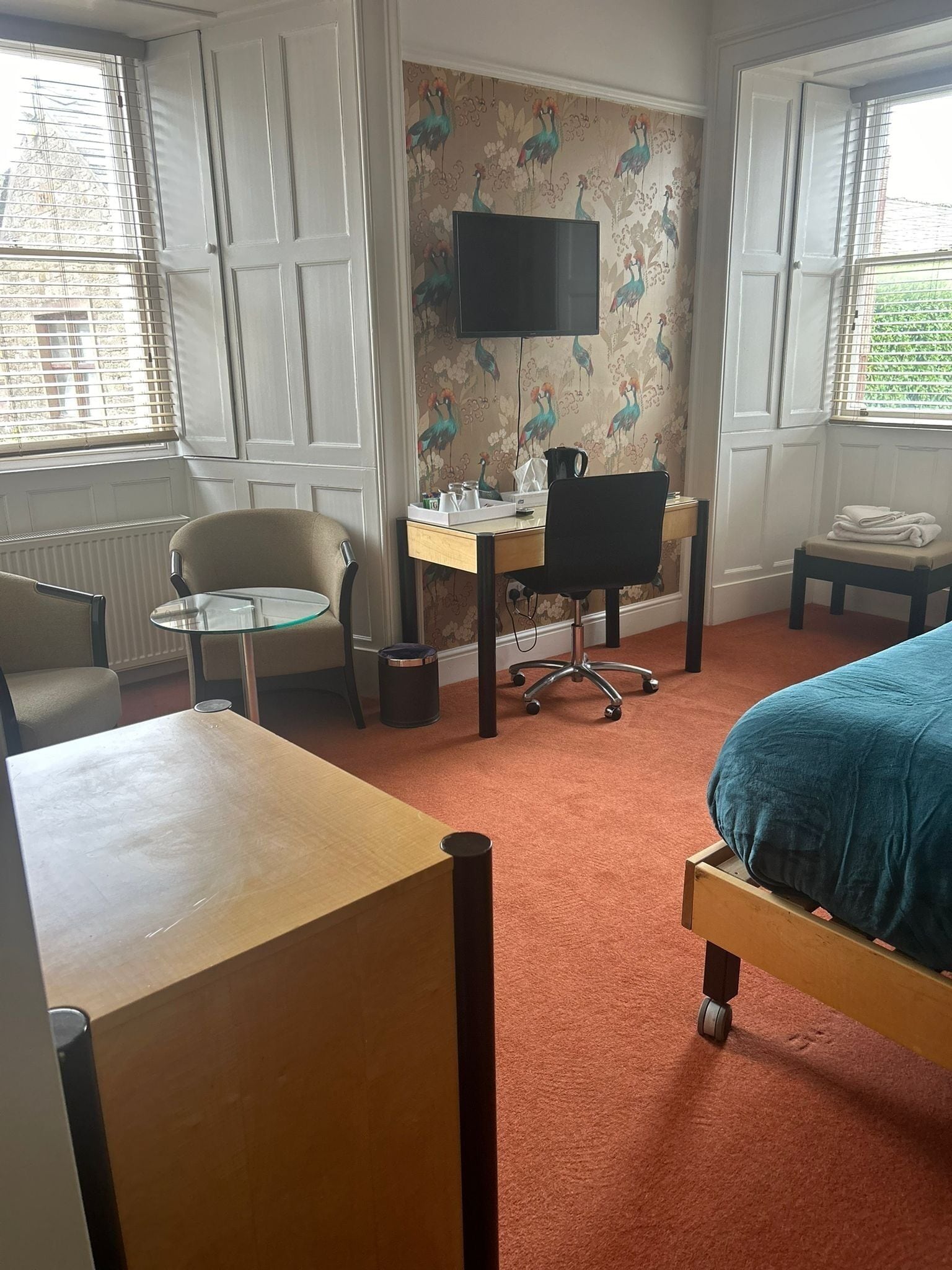 A hotel room with a bed, a desk, a chair, a TV, and a window with blinds.