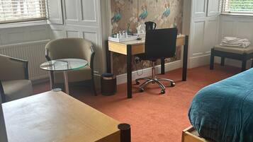 A hotel room with a bed, a desk, a chair, a TV, and a window with blinds.