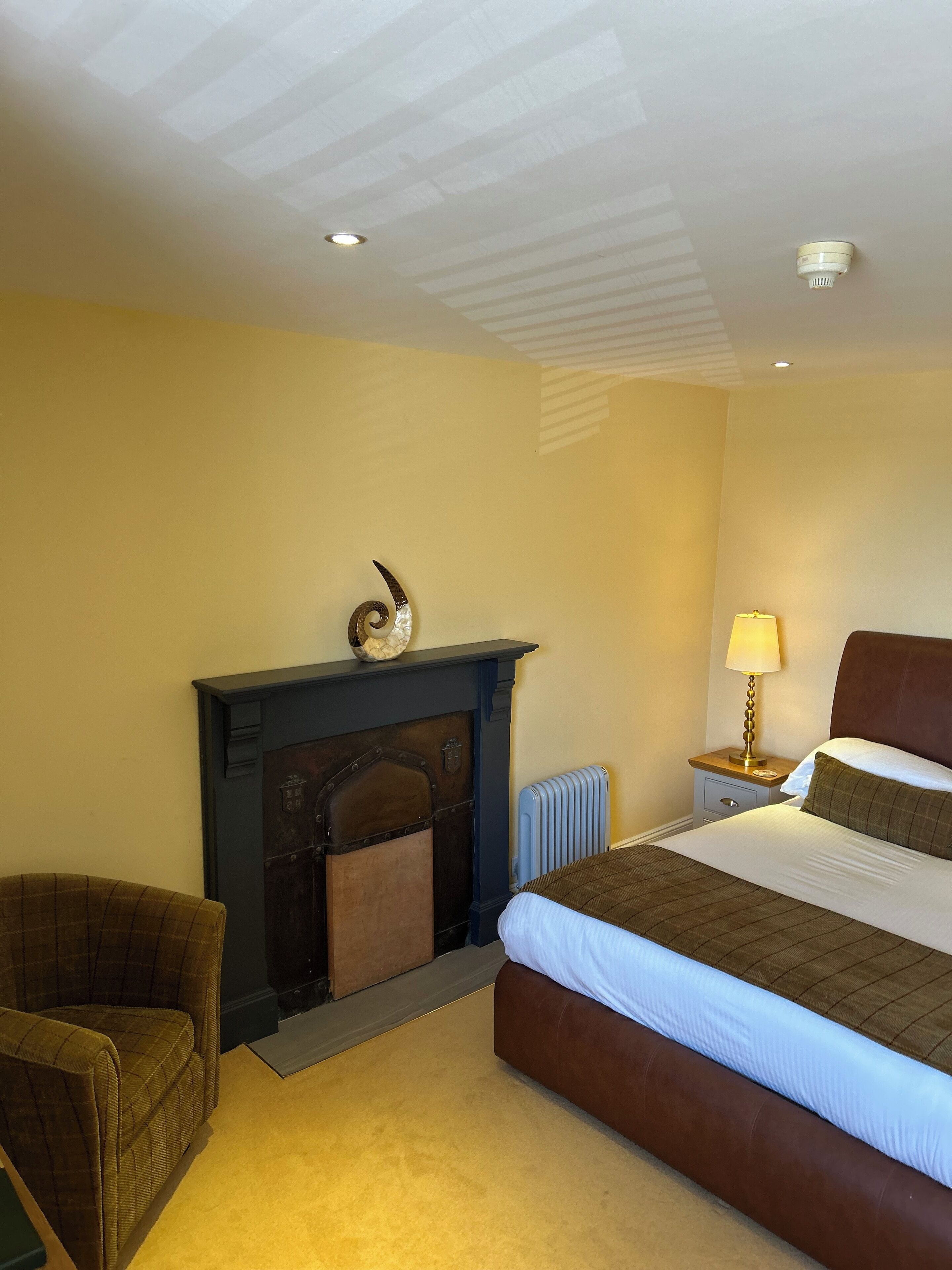 A hotel room with a bed, a fireplace, a nightstand with a lamp, and a chair.