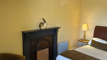 A hotel room with a bed, a fireplace, a nightstand with a lamp, and a chair.