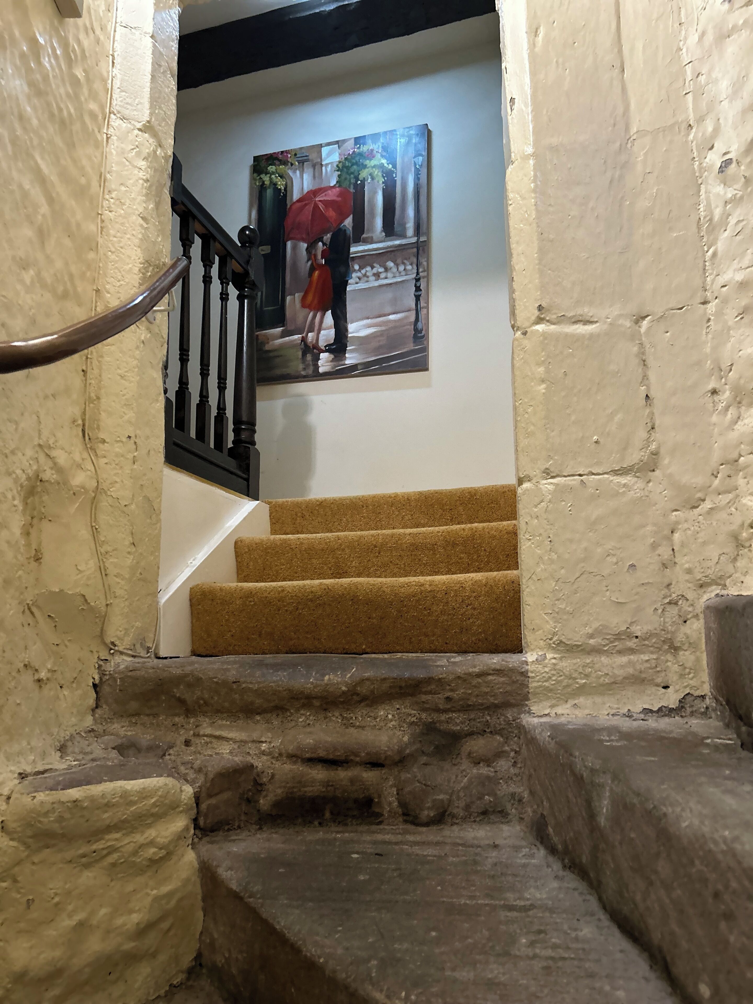 Una escalera de piedra con barandilla, que conduce a una habitación con un cuadro de una pareja bajo un paraguas.