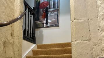 Una escalera de piedra con barandilla, que conduce a una habitación con un cuadro de una pareja bajo un paraguas.
