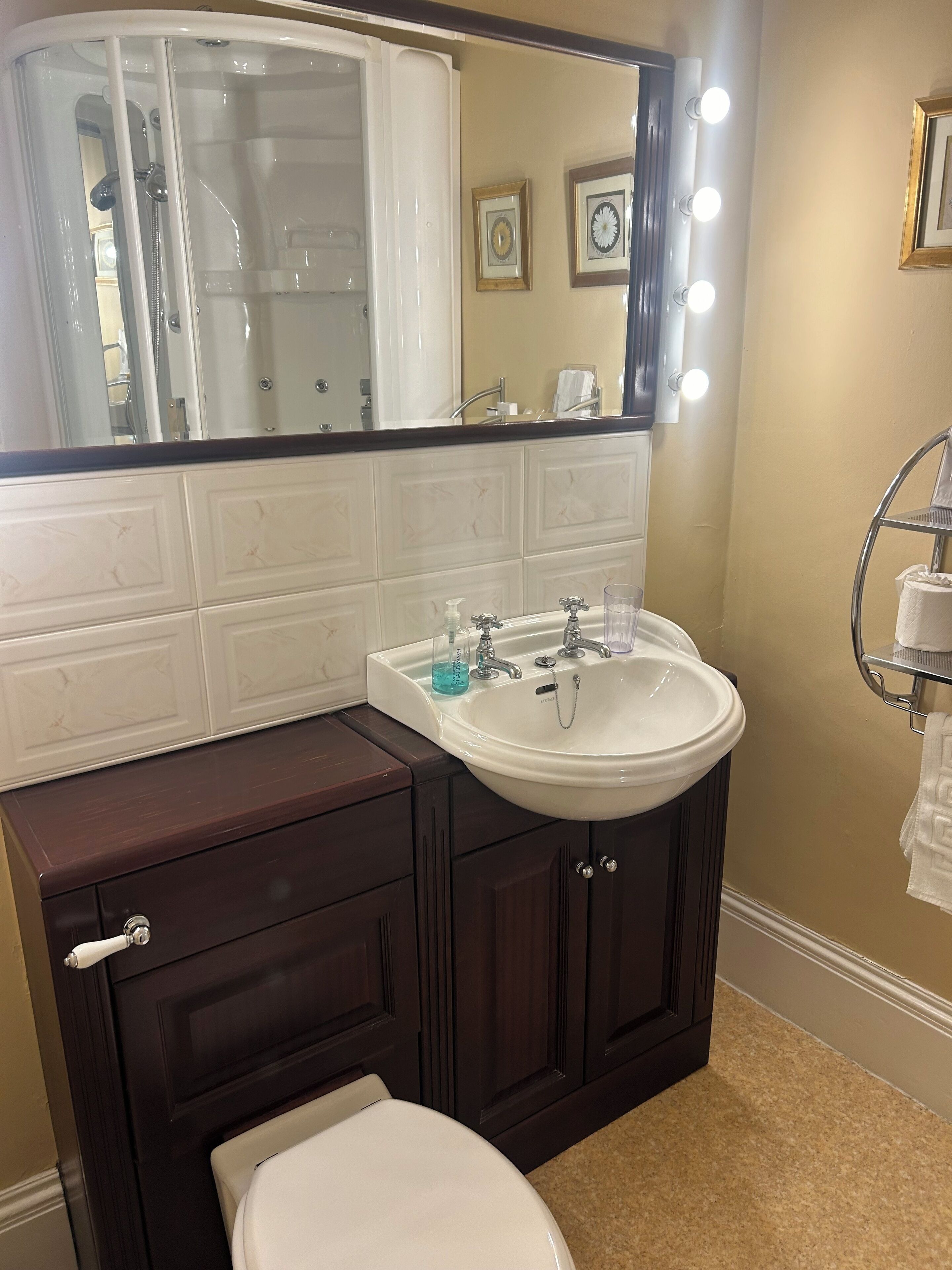A bathroom with a white sink, dark wooden vanity, and a mirror with lights.
