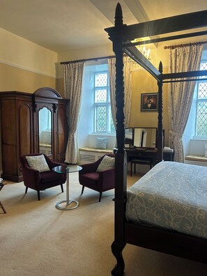 A four-poster bed with a wooden headboard, two armchairs with patterned cushions, a small round table, and a large wooden wardrobe. - Moresby Hall (Whitehaven)