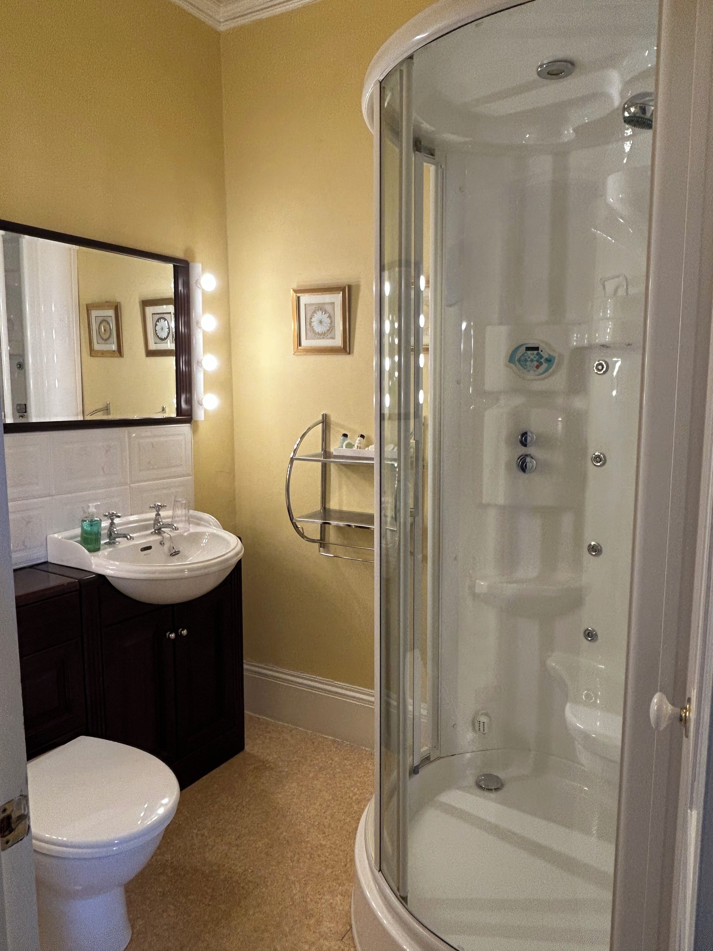 Un baño con lavamanos blanco, un espejo con iluminación, inodoro y ducha con mampara de vidrio.