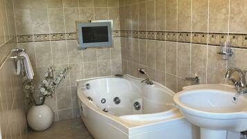 Une salle de bain avec une grande baignoire, un lavabo et un téléviseur fixé au mur.