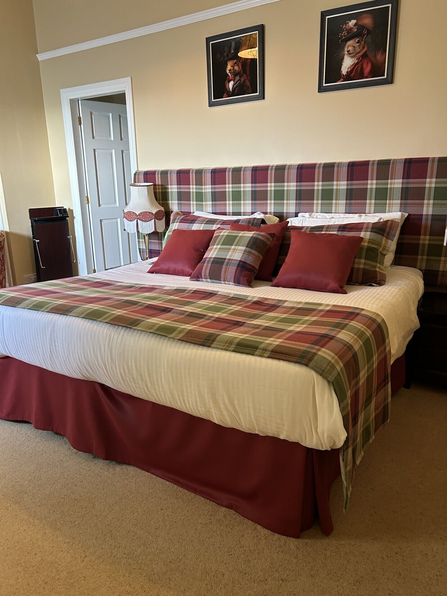 Una camera da letto con copripiumino a quadri, numerosi cuscini, una testiera a motivi tartan e due quadri appesi al muro.