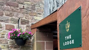 A wooden door with a sign reading "THE LODGE" and a hanging flower basket. - Moresby Hall (Whitehaven)