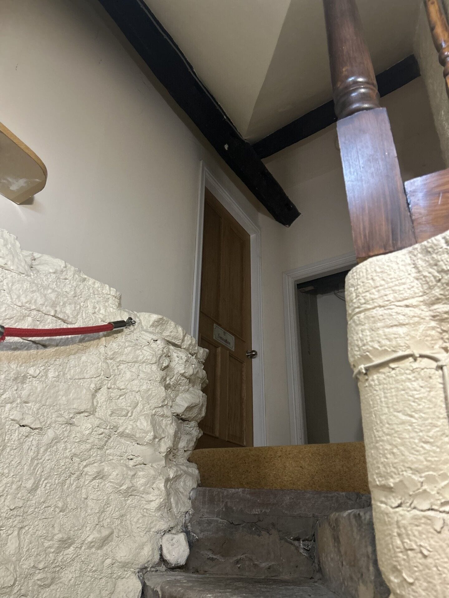 A staircase with a textured wall, a wooden door, and a red object on the wall.