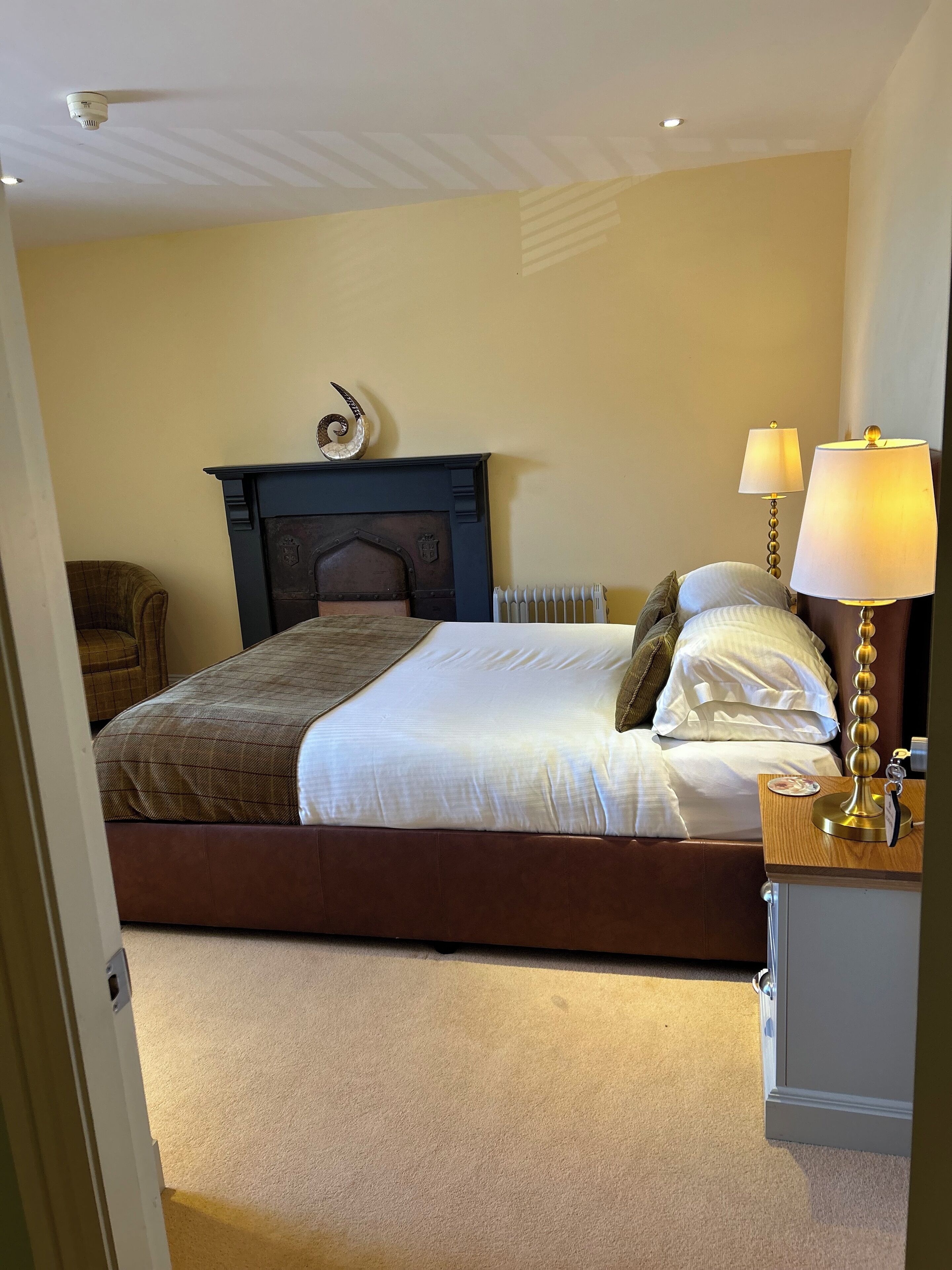 A bedroom with a bed, two bedside lamps, a radiator, and a decorative wall piece.