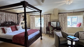 A four-poster bed with a red bedspread, a desk with a chair, and a sofa with patterned cushions in a well-lit room with large windows. - Moresby Hall (Whitehaven)