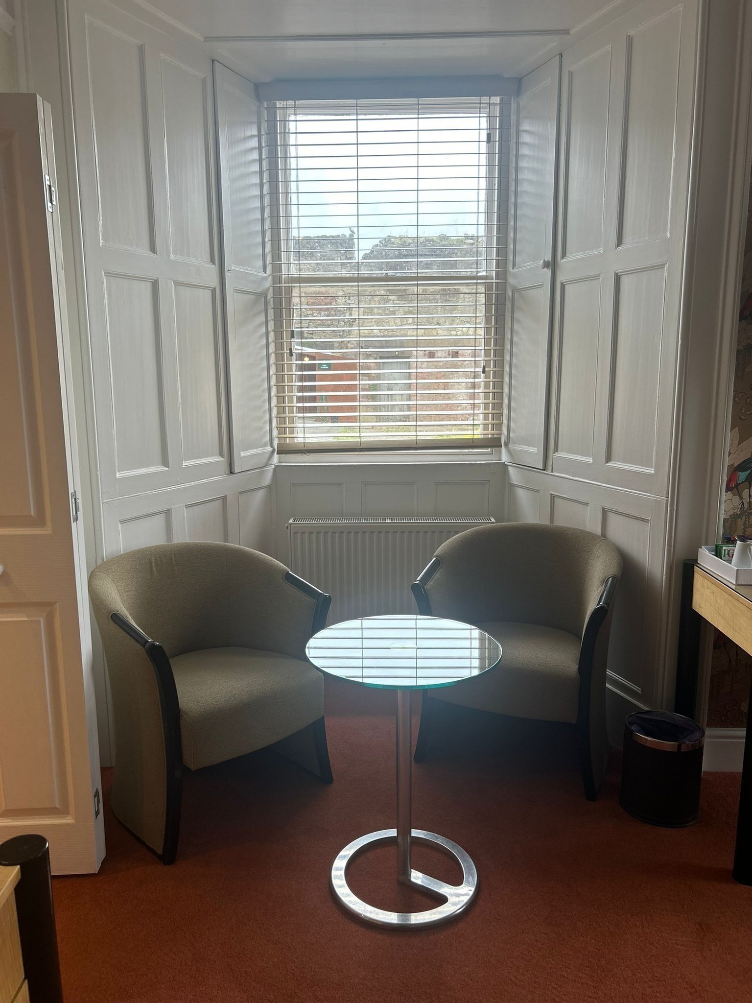 A corner room with two chairs, a small table, and a window with blinds.