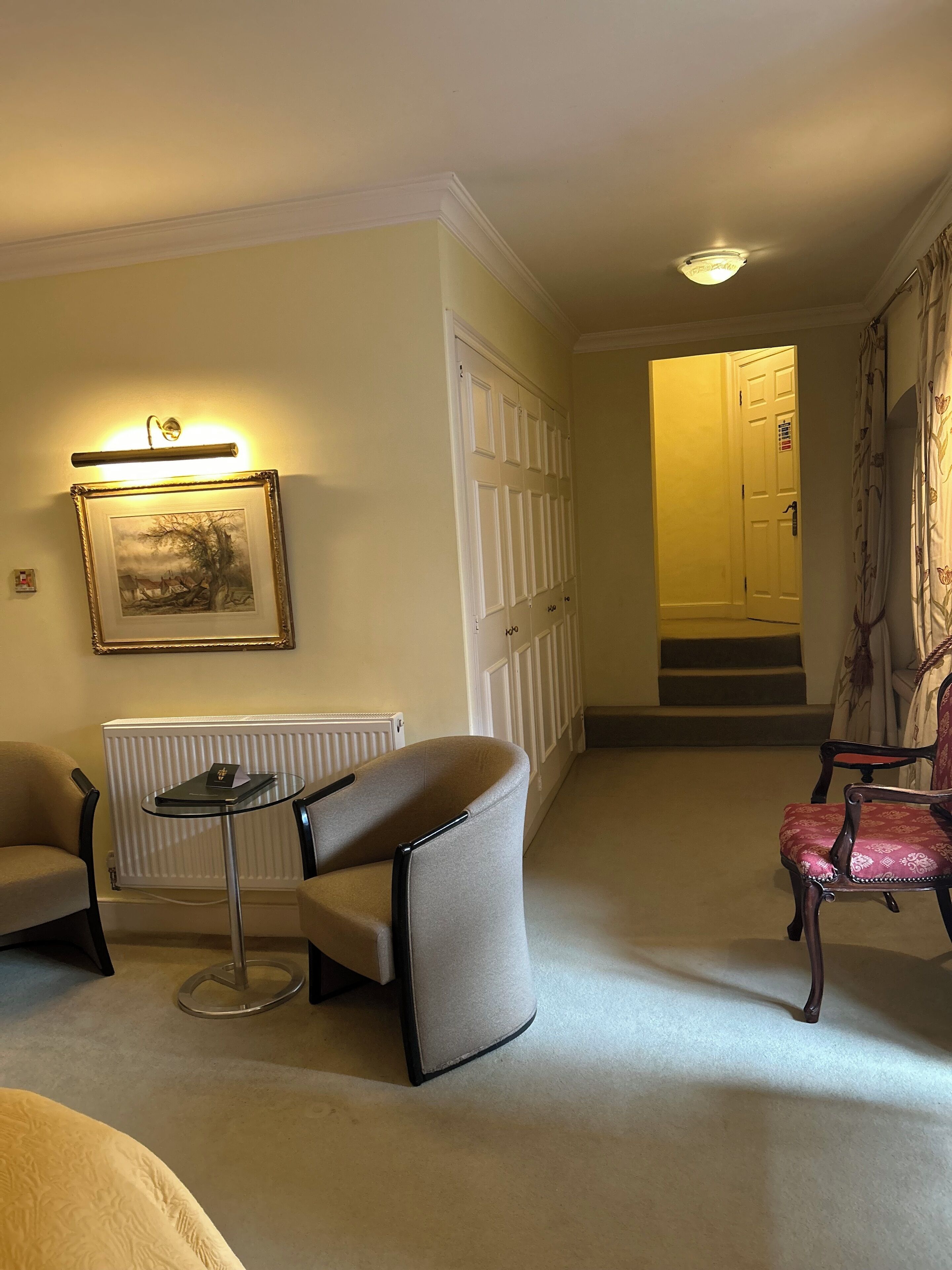 A hotel room with a seating area featuring a table and two chairs, a framed artwork on the wall, and a door leading to a staircase.
